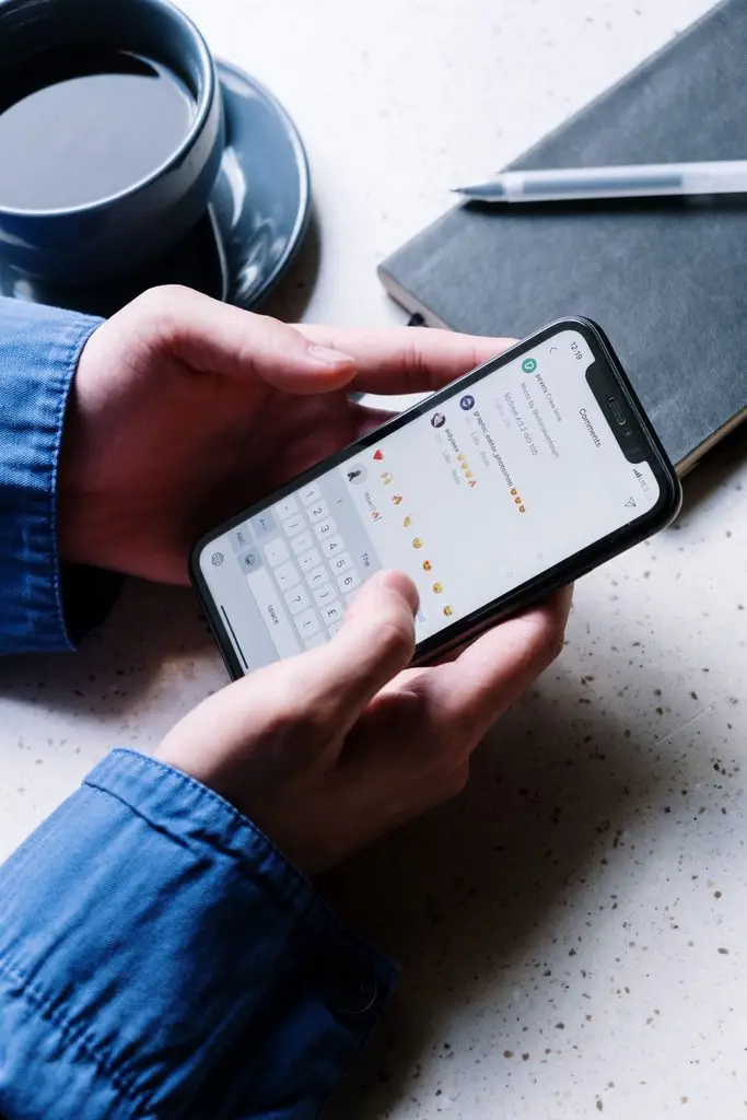 Hands typing a reply in Instagram comments on a smartphone beside a coffee cup and notebook.