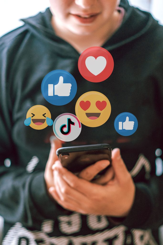 Person smiling at their phone as likes, hearts, emoji reactions, and a TikTok icon float above it.