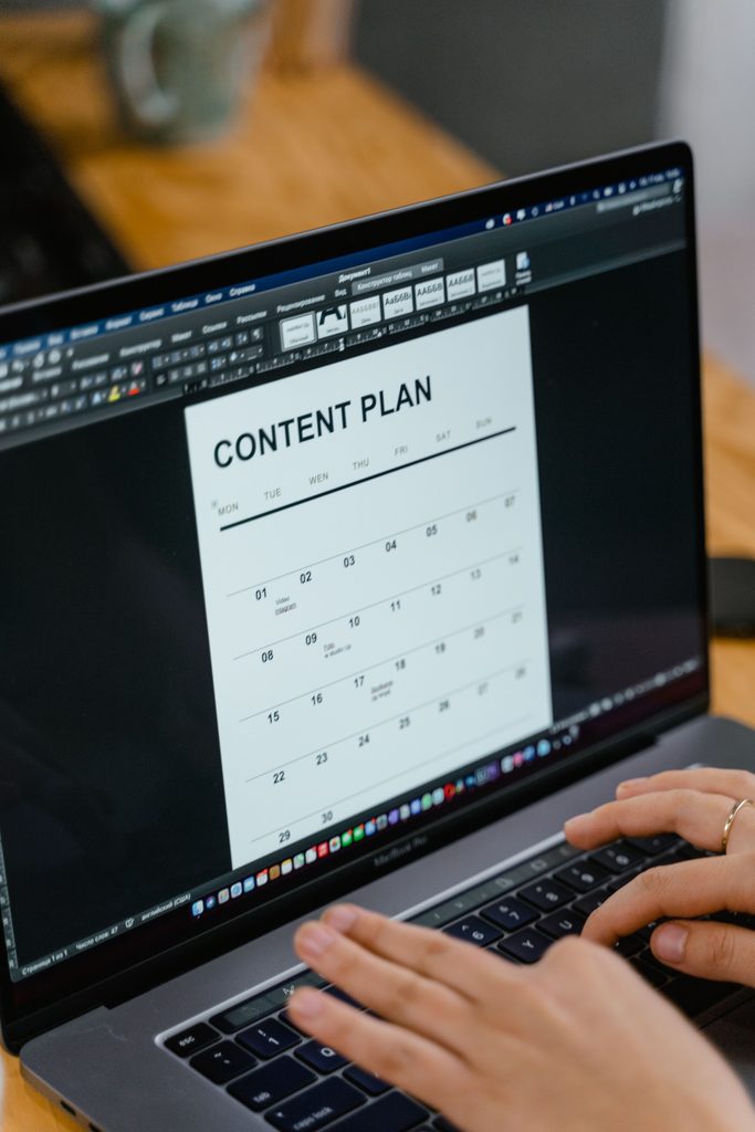 Hands typing on a laptop showing a monthly social media content plan calendar.