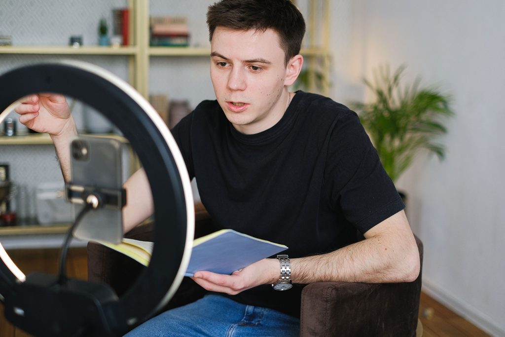 Content creator reading from notes while recording a social media video on a phone with a ring light.